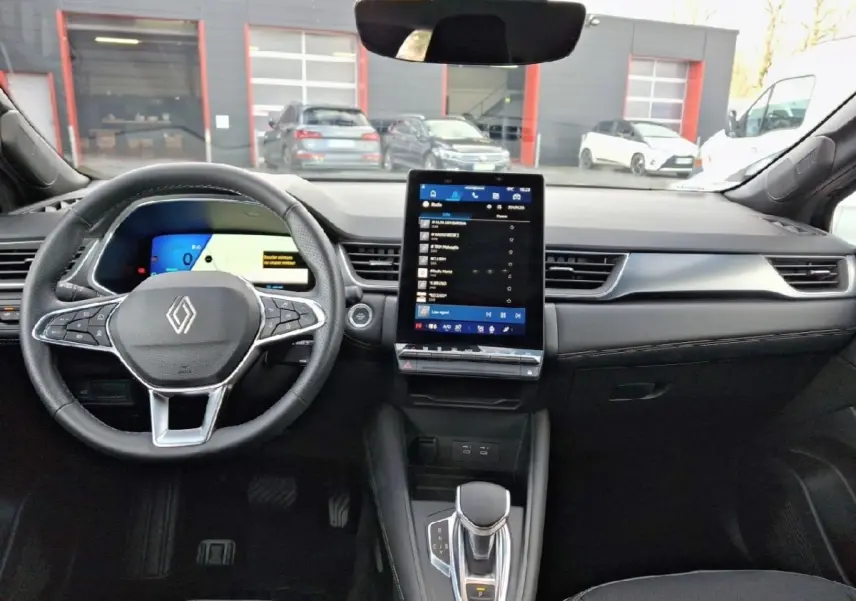 Vue intérieure avant du tableau de bord noir de la Renault SYMBIOZ avec écran tactile vertical et volant multifonctions.