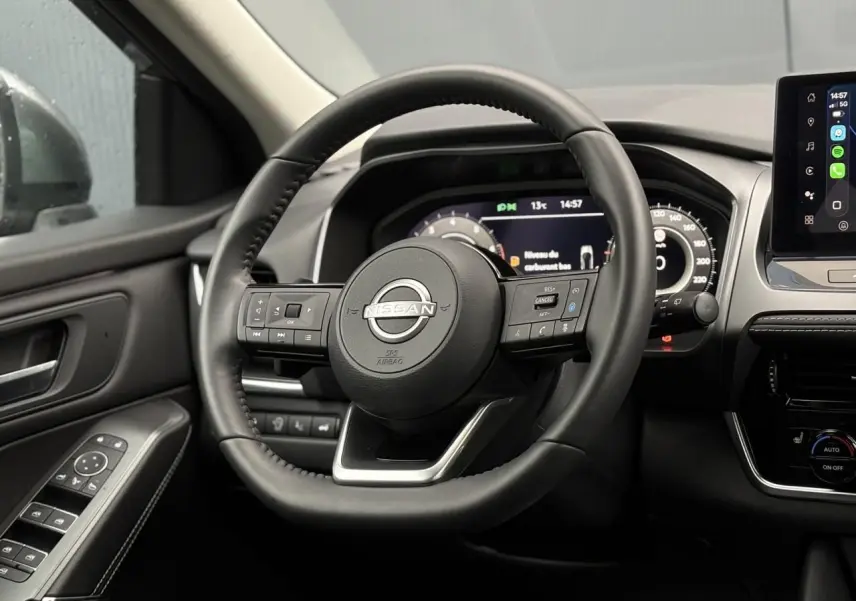 Vue intérieure centrée sur le volant cuir noir du Nissan Qashqai 2024 avec tableau de bord numérique et écran tactile.