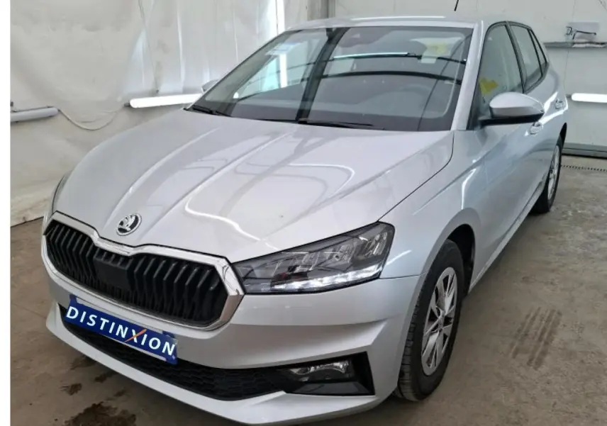 Vue 3/4 avant droite d'une Skoda Fabia Ambition gris clair 2023 avec calandre noire et phares LED allumés.