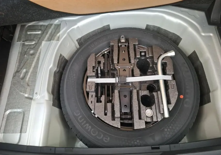 Vue plongeante sur la roue de secours grise avec outils de bord dans le coffre d'une Skoda Fabia Ambition 2023.