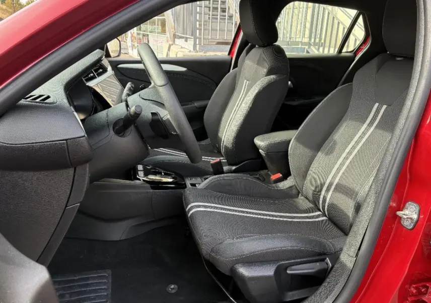 Vue intérieure côté conducteur de l’Opel Corsa 2025 rouge peperoncino, avec sièges tissu noirs à bandes grises.