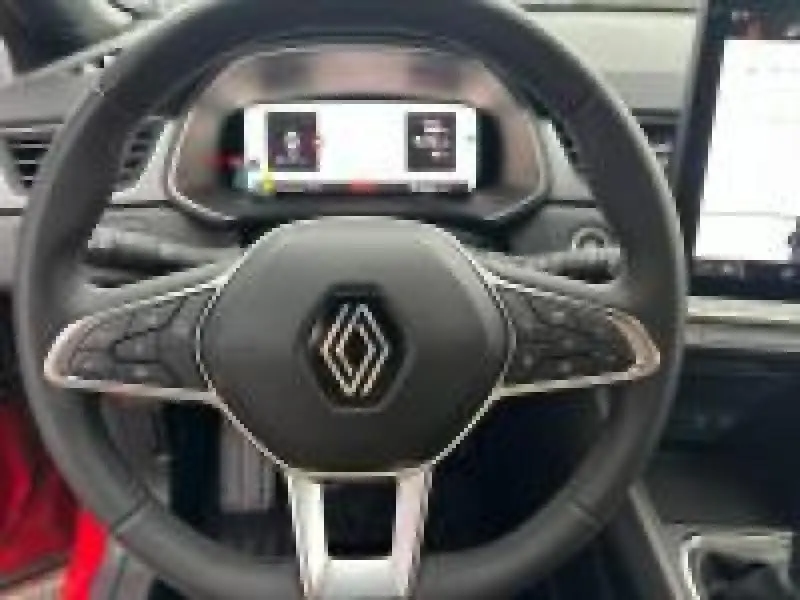 Vue rapprochée du volant multifonction noir avec logo Renault au centre, tableau de bord numérique et écran tactile du Renault Captur rouge.