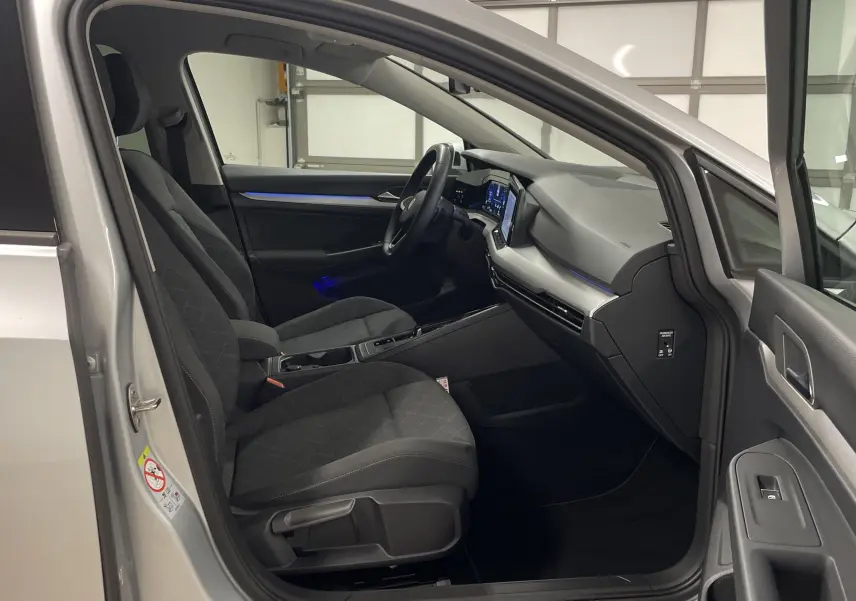 Intérieur avant droit d'une Volkswagen Golf 2022 argent avec sièges noirs et tableau de bord numérique éclairé.