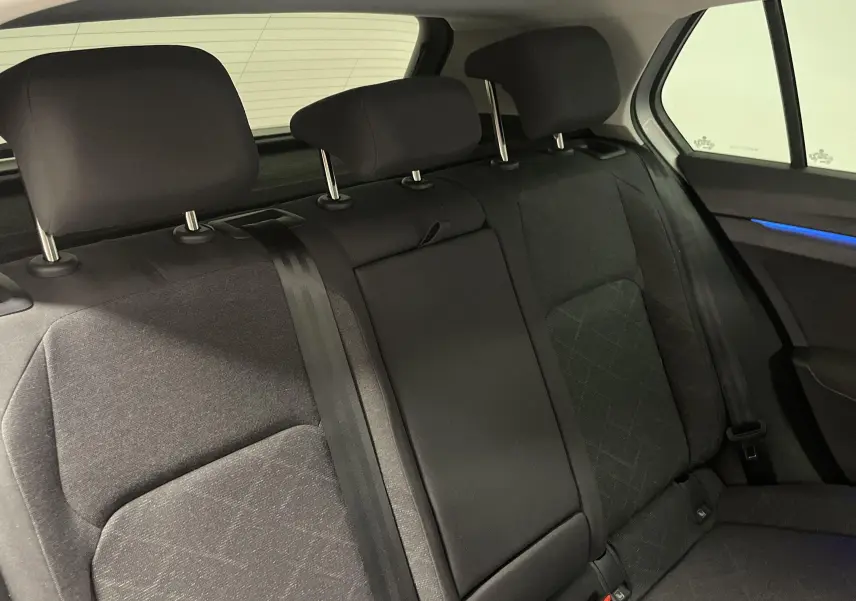 Vue intérieure des sièges arrière noirs de la Volkswagen Golf 2.0 TDI 115 DSG7 avec éclairage d'ambiance bleu sur la porte.
