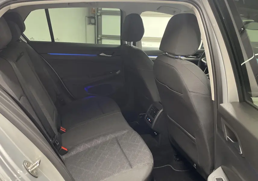 Vue intérieure arrière côté droit de la Volkswagen Golf 2.0 TDI 115 argent avec sièges tissu noirs et éclairage d'ambiance bleu.