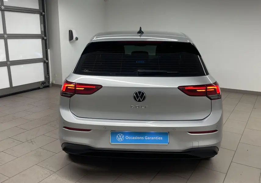 Vue arrière d'une Volkswagen Golf 2022 couleur reflet d'argent avec feux allumés dans un garage.