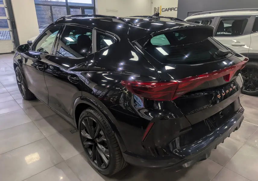 Vue 3/4 arrière droite du CUPRA Formentor eHybrid noir minuit avec feux arrière continus et jantes noires en showroom.