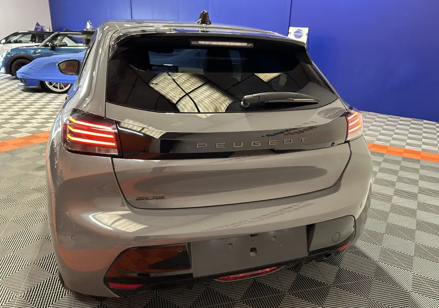 Vue arrière d'une Peugeot 208 gris Selenium avec feux LED allumés dans un showroom intérieur.
