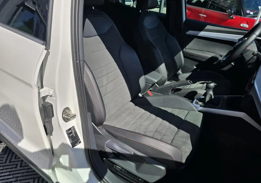 Vue intérieure côté conducteur du SEAT Arona blanc toit noir 2024, sièges en suédine noire avec surpiqûres rouges et boîte manuelle.