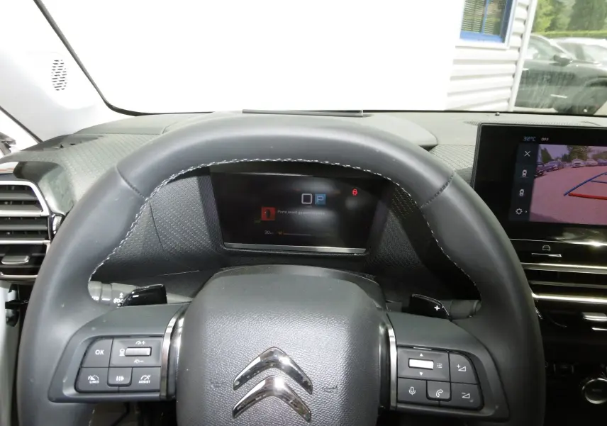 Vue rapprochée du volant et du tableau de bord numérique d'une Citroën C4 X blanche, avec écran multimédia affichant la caméra de recul.