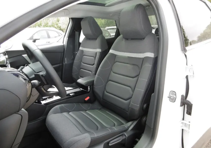 Vue intérieure côté conducteur d'une Citroën C4 X blanche, sièges bi-matière gris et noir avec surpiqûres bleues.