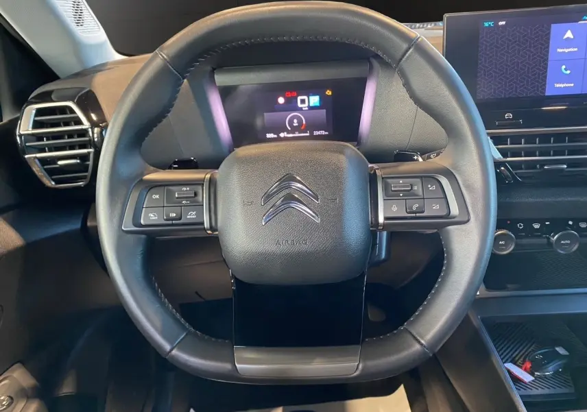 Vue frontale du volant noir de la Citroën C4 BlueHDi 130 Plus 2023 avec commandes intégrées et tableau de bord numérique.