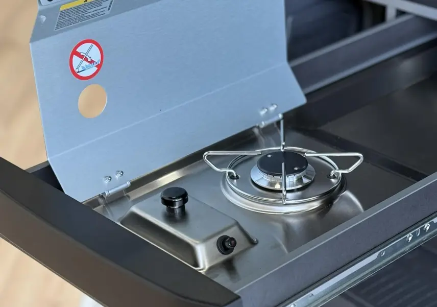 Gros plan sur le réchaud à gaz extensible en inox de la mini-cuisine du Volkswagen California T7 blanc Candy.