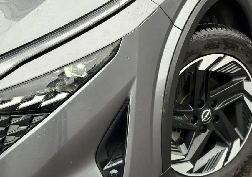 Gros plan sur l'avant droit gris Squale du Nissan Qashqai 2024, mettant en valeur le phare LED et la jante alliage 18 pouces.