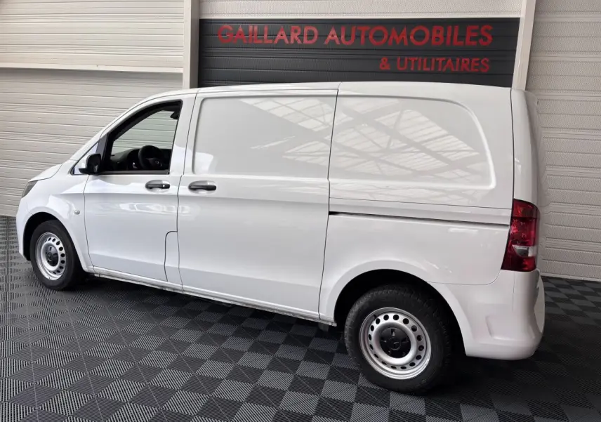 Vue latérale droite d'un utilitaire Mercedes Vito 111 CDI Compact blanc avec deux portes et hayon, en intérieur showroom.