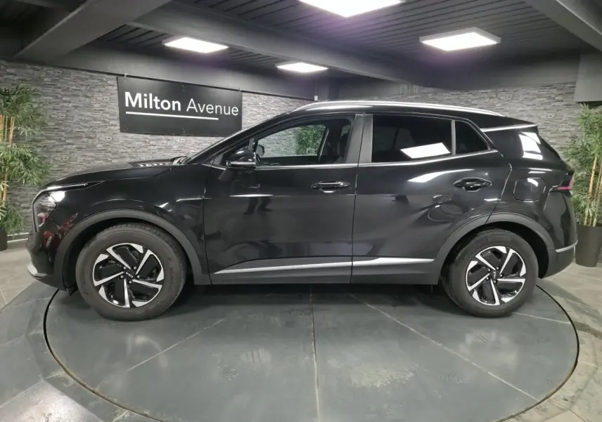 Profil côté gauche du SUV KIA SPORTAGE noir métallisé avec jantes alliage et détails chromés en intérieur showroom.