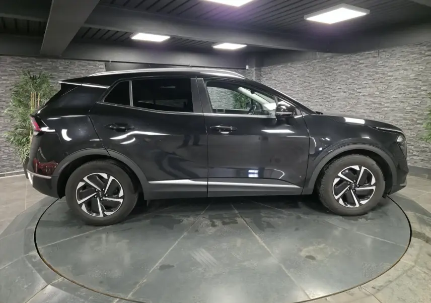 Profil côté gauche du SUV KIA SPORTAGE noir 2022 avec jantes alliage et vitres teintées dans un showroom.
