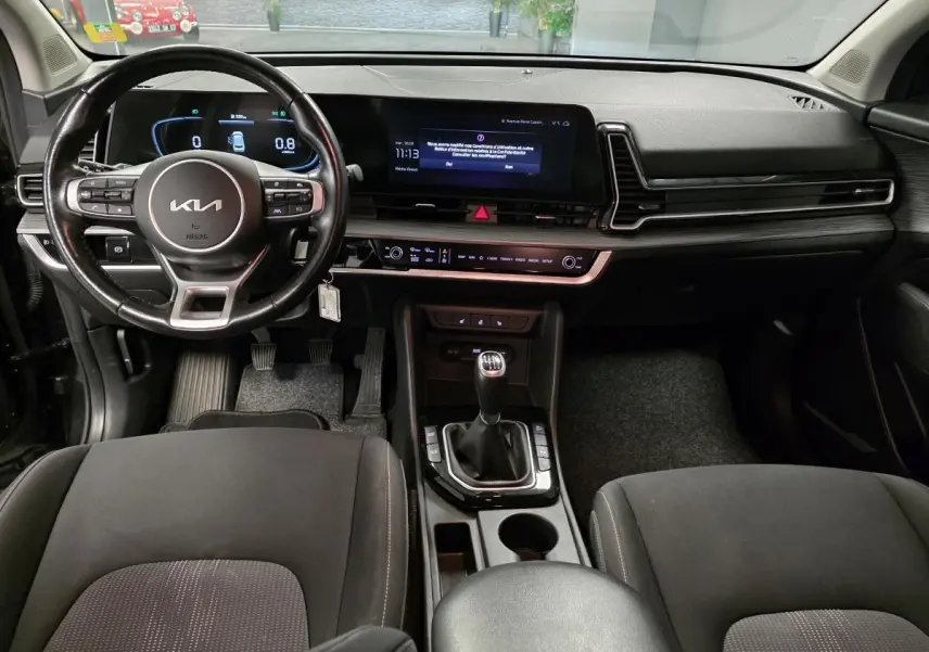 Intérieur noir du Kia Sportage 2022 vu de face, volant cuir, tableau de bord numérique et levier de vitesse manuel.