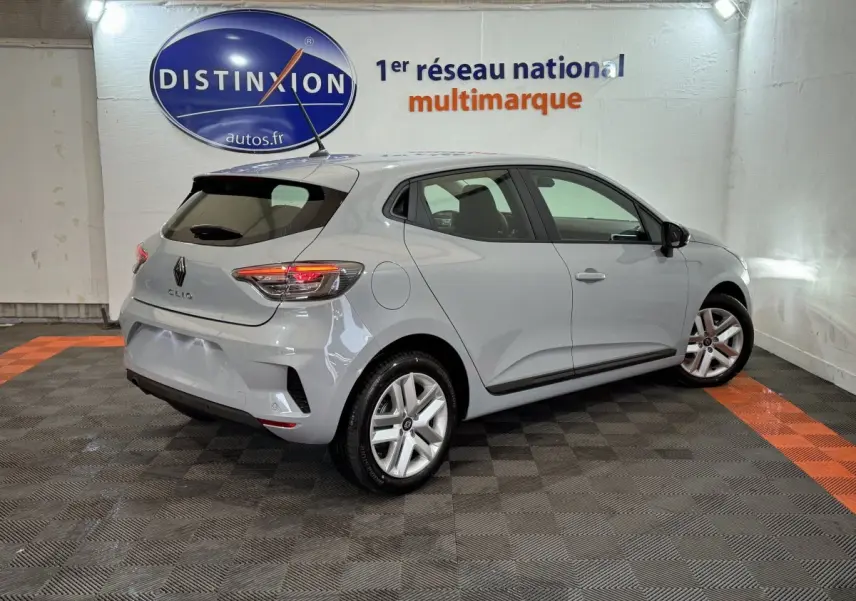 Renault Clio gris clair vue 3/4 arrière droit dans un showroom avec feux arrière allumés et jantes alliage.