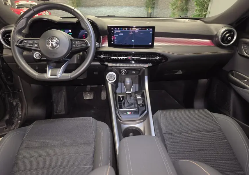 Vue intérieure avant de l'Alfa Romeo Tonale 2023, tableau de bord noir avec écran tactile et volant sport cuir.