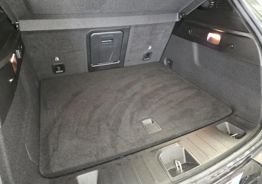 Coffre ouvert de l'Alfa Romeo Tonale gris, vue plongeante sur le tapis de sol et les rangements latéraux.