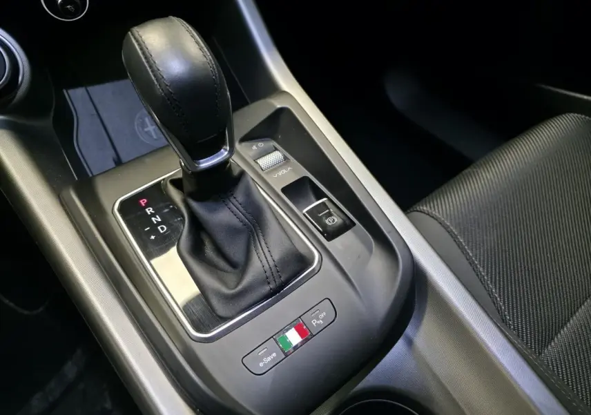 Gros plan sur la console centrale de l'Alfa Romeo Tonale gris, avec levier de vitesse automatique et bouton aux couleurs italiennes.