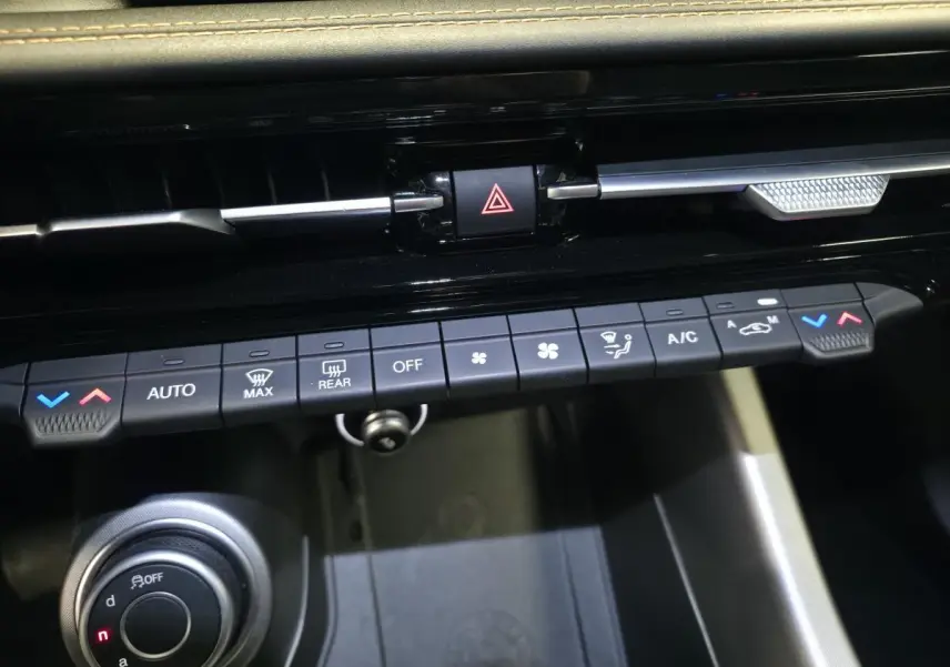 Vue rapprochée de la console centrale de l'Alfa Romeo Tonale grise, montrant les commandes de climatisation et le bouton de sélection de mode de conduite.