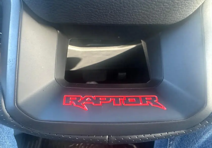 Gros plan sur le logo rouge RAPTOR sur la console centrale noire du Ford Ranger Raptor 2025, intérieur moderne.