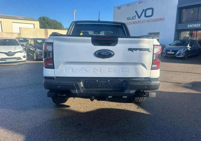 Vue arrière d'un Ford Ranger Raptor blanc 2025 avec logo Ford et inscription RANGER en relief sur la benne.