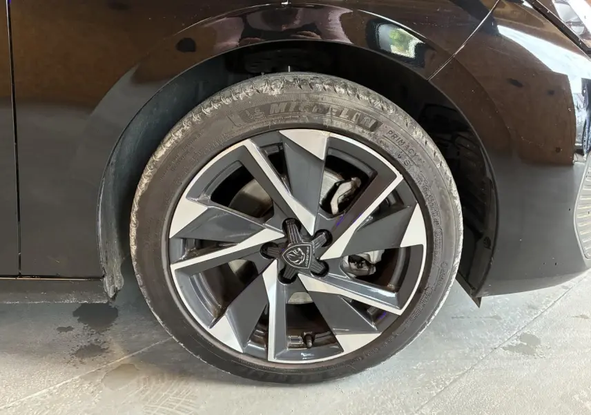 Gros plan sur la roue avant gauche de la Peugeot 308 SW noire, jante alliage 17'' Halong diamantée avec logo Peugeot central.