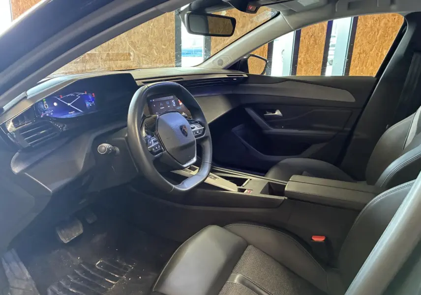 Intérieur de la Peugeot 308 SW 2024 vu côté conducteur, avec tableau de bord numérique et sellerie noire.