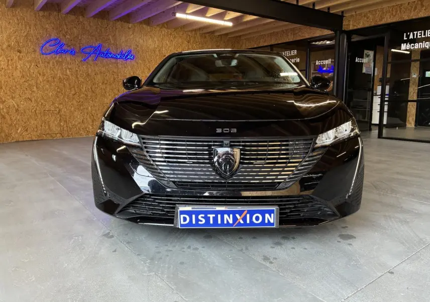 Vue avant d'une Peugeot 308 SW noire 2024 avec calandre noire et logo lion chromé, en intérieur showroom.