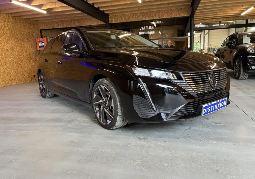 Peugeot 308 SW noire vue 3/4 avant droit en intérieur avec calandre chromée et jantes alliage.