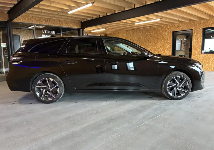 Peugeot 308 SW noire vue de profil côté gauche dans un garage avec jantes alliage et vitres teintées.