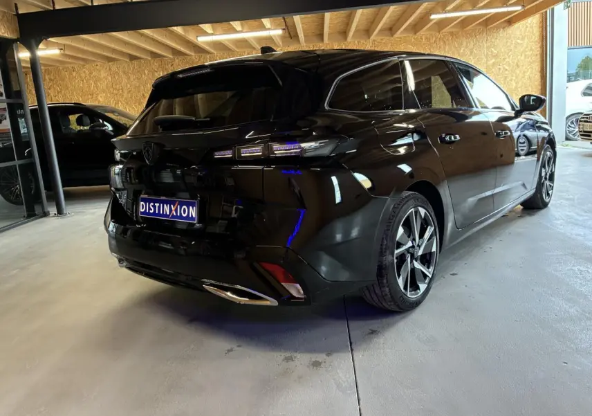 Peugeot 308 SW noire vue 3/4 arrière droit dans un showroom avec feux arrière LED et jantes alliage.