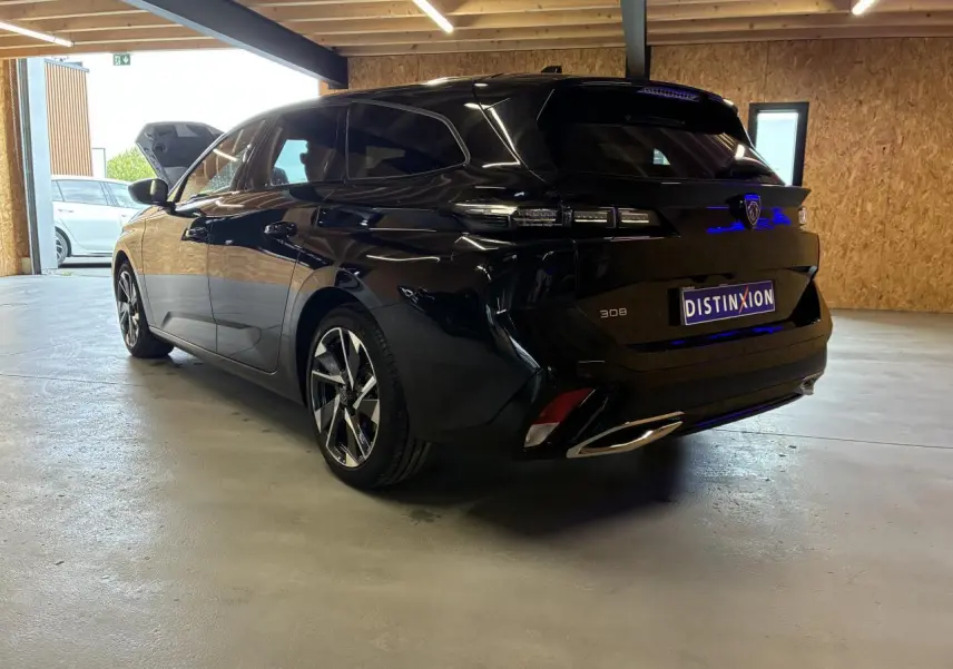 Peugeot 308 SW noire vue 3/4 arrière droit en intérieur, avec jantes alliage et feux arrière LED distinctifs.