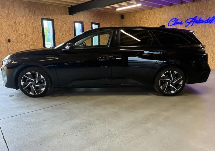 Peugeot 308 SW noire vue de profil droit dans un garage avec jantes alliage et vitres surteintées.
