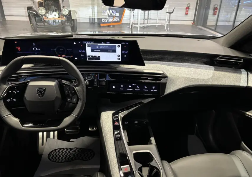 Vue intérieure avant de la Peugeot 3008 GT 2025, tableau de bord gris clair avec écran panoramique incurvé et volant compact noir.
