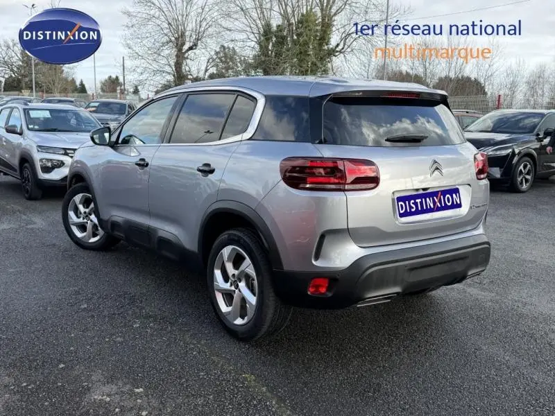 Vue 3/4 arrière droite d'un Citroën C5 Aircross gris 2024 avec toit noir et feux arrière distinctifs, stationné en extérieur.