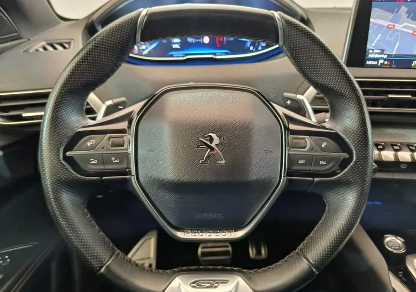 Vue rapprochée du volant cuir perforé noir avec logo Peugeot et tableau de bord numérique du 5008 GT gris clair.