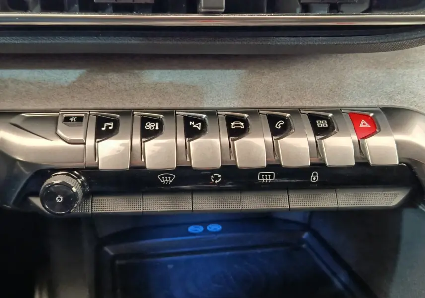 Gros plan sur la rangée de boutons métalliques et rouges du tableau de bord du Peugeot 5008 gris clair, version GT.