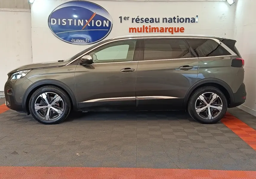 Vue de profil côté gauche d’un Peugeot 5008 GT gris clair stationné en intérieur avec jantes alliage et vitres teintées.