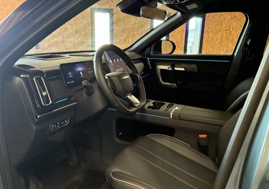 Vue intérieure côté conducteur du JAECOO J7 2026, avec sellerie cuir noire et éclairage d'ambiance bleu subtil.