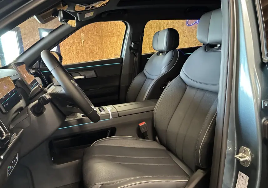 Vue intérieure côté conducteur du JAECOO J7 2026, sièges cuir noir avec éclairage d'ambiance bleu subtil.