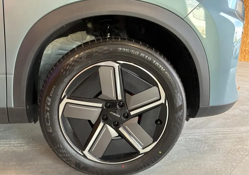Gros plan sur la jante alliage 19 pouces noire et grise du SUV JAECOO J7 gris olive, avec logo central visible.