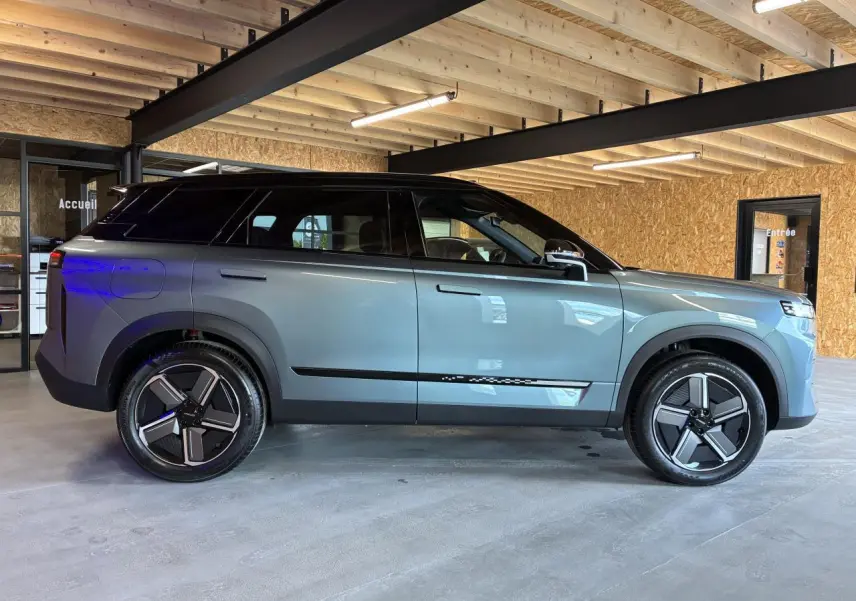SUV JAECOO J7 2026 gris olive avec toit noir, vu de profil côté gauche dans un garage lumineux.