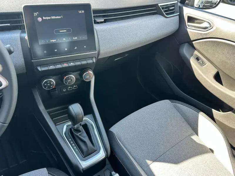 Intérieur avant droit de la Renault Clio 2025 avec console centrale, écran tactile et sellerie textile gris motif 3D.