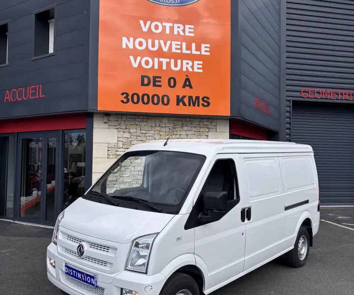 Vue 3/4 avant d'un utilitaire blanc DFSK EC35 BEV 39KWH VAN garé devant un bâtiment commercial.