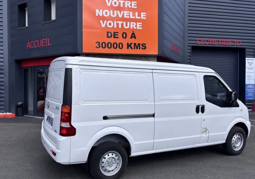 Vue 3/4 arrière droite d'un utilitaire blanc DFSK EC35 BEV 39KWH, stationné devant un bâtiment commercial.