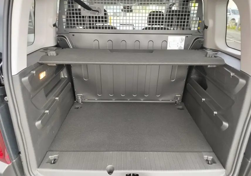 Coffre ouvert vu de l'arrière d'un Citroën Berlingo noir Perla Nera, avec séparation grillagée et tablette de rangement.